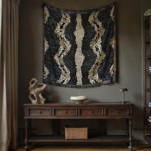 Peut inclure: Une tenture murale sombre &agrave; motifs, avec une bordure &agrave; franges, est suspendue au-dessus d'une console en bois. La tenture pr&eacute;sente un motif r&eacute;p&eacute;titif de formes bleu fonc&eacute;, beige et blanches. La console a trois tiroirs et une &eacute;tag&egrave;re inf&eacute;rieure avec un panier tress&eacute;.