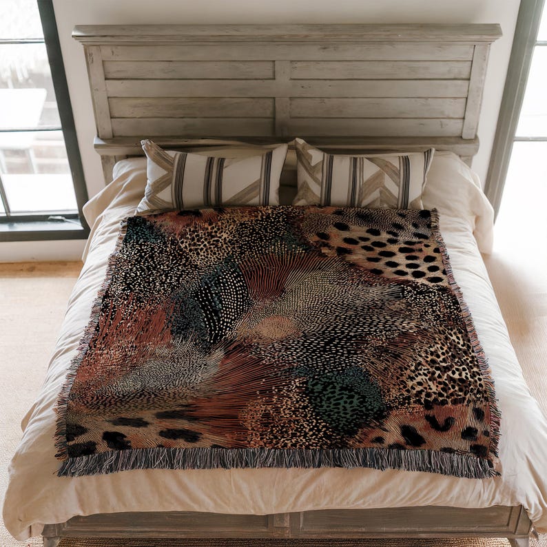 Op de afbeelding: Een rechthoekige geweven plaid met een complex, meerkleurig patroon van dierenprints, gespikkelde texturen en abstracte vormen in tinten zwart, bruin, roest en groenblauw, afgewerkt met een gefranjerde rand aan de boven- en onderkant.