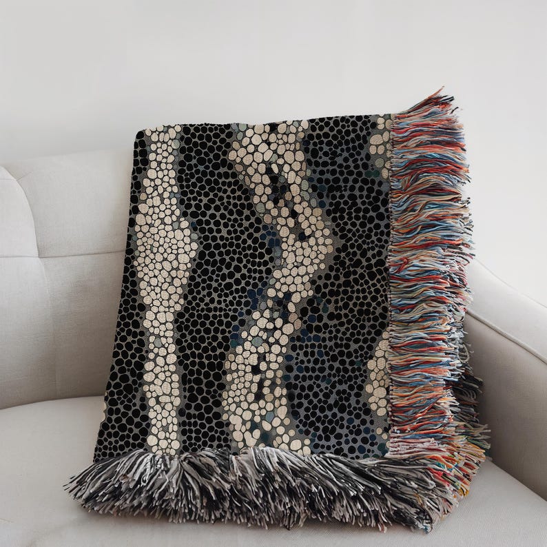Peut inclure: Une couverture d&eacute;corative avec un motif unique de petites formes circulaires en noir, blanc cass&eacute; et bleu. La couverture a un bord &agrave; franges multicolores et est drap&eacute;e sur un canap&eacute; blanc.