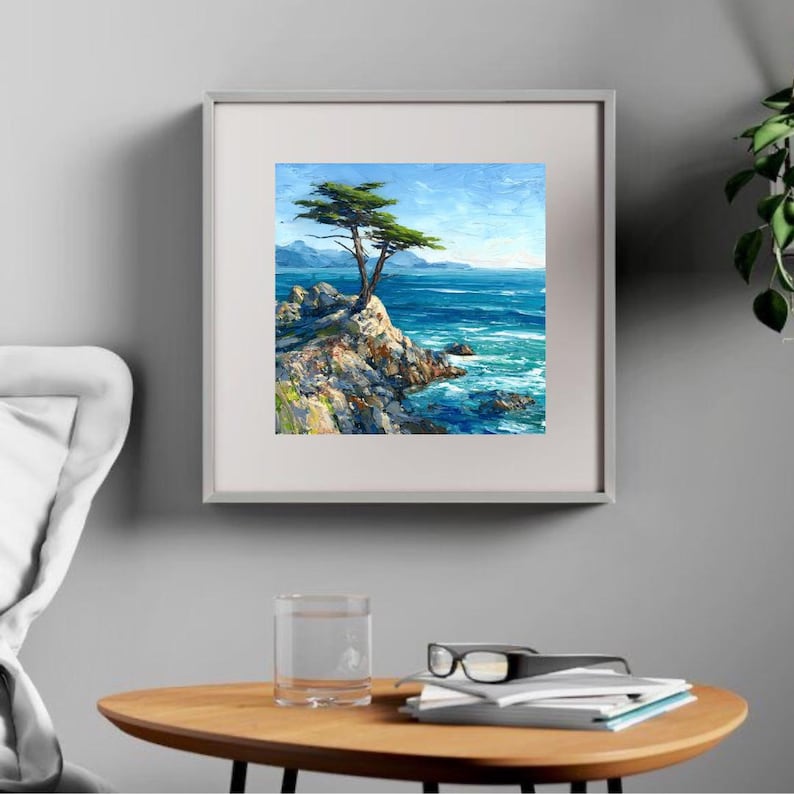 May include: Framed landscape painting of a coastal scene. A lone tree stands on a rocky cliff overlooking the turquoise ocean. The sky is a bright blue with hints of clouds. The painting is in a silver frame.