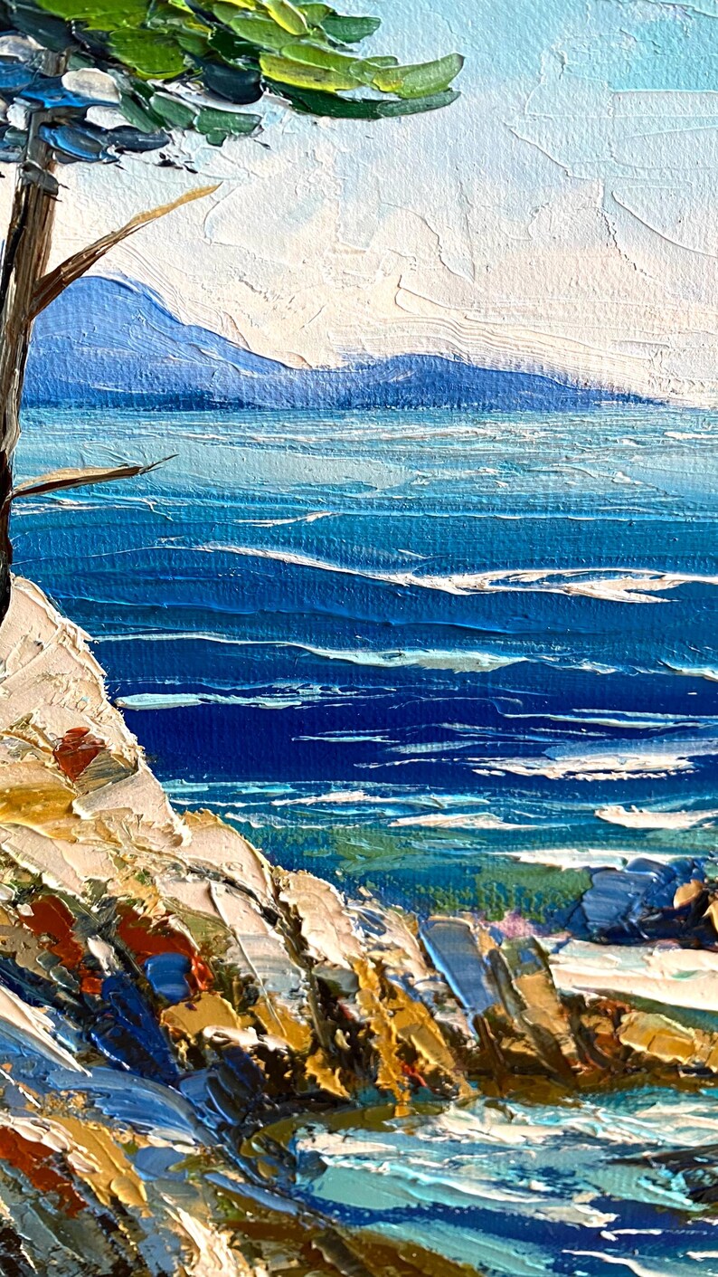 May include: Impasto oil painting of a coastal scene. The artwork depicts a vibrant blue ocean with white-capped waves, a rocky shoreline, and a tree. The sky is a light blue. The painting uses thick brushstrokes to create texture and depth.