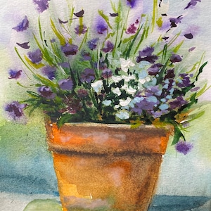 Può includere: Un vaso di terracotta pieno di fiori viola e bianchi. Il vaso è appoggiato su una superficie verde.
