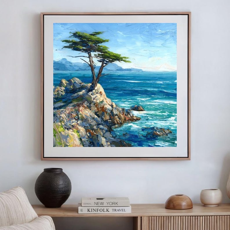 May include: Oil painting of a coastal landscape featuring a tree on a rocky cliff overlooking the ocean. The artwork has a textured appearance with shades of blue, green, and white, framed in a light wood frame.