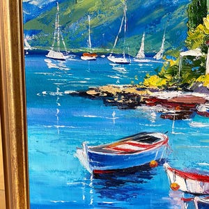 May include: Oil painting of a coastal scene with sailboats and small boats. The artwork features a vibrant blue sea, green hills, and a golden frame. The boats are blue and white with red accents.