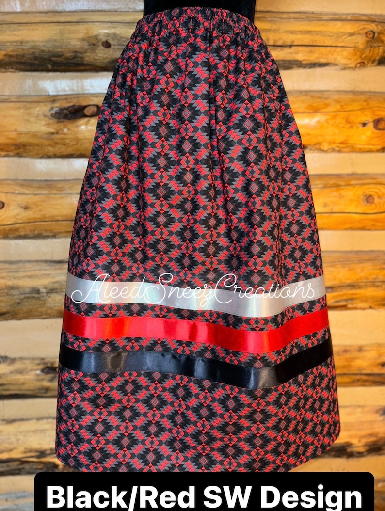 Pode incluir: Uma saia com um padr&atilde;o geom&eacute;trico preto e vermelho e uma cintura el&aacute;stica. A parte inferior inclui tr&ecirc;s faixas horizontais de fita em prata, vermelho e preto. O texto AteedSneezCreations &eacute; vis&iacute;vel no meio e Black/Red SW Design est&aacute; impresso na parte inferior.