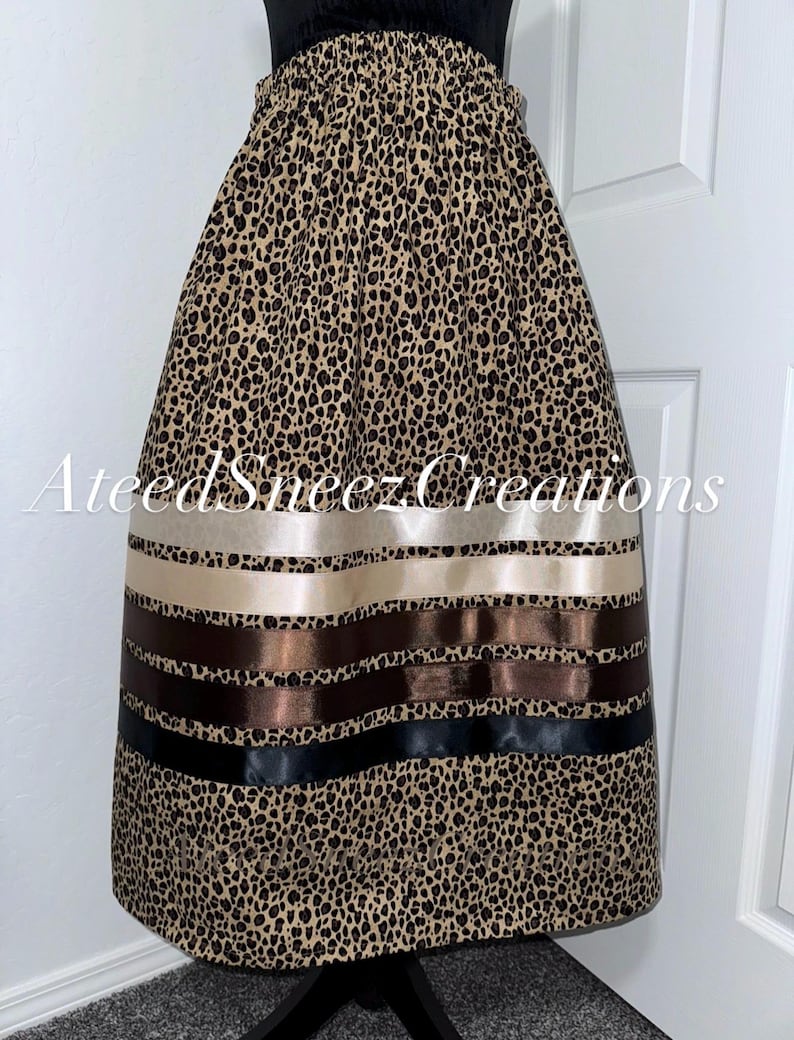 K&ouml;nnte beinhalten: Ein Rock mit einem beigefarbenen und schwarzen Leopardenmuster und einem elastischen Bund. Der untere Teil ist mit vier horizontalen Satinb&auml;ndern in den Farben Creme, Hellbraun, Dunkelbraun und Schwarz verziert. Der Text AteedSneezCreations ist sichtbar.