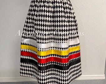 May include: A midi-length skirt featuring a black and white diamond pattern with a gathered elastic waistband. The lower section includes horizontal bands of white, yellow, red, and black ribbon trim. The text AteedSheezCreations is visible.