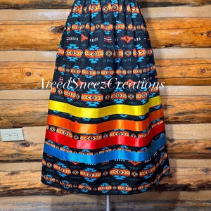 Pode incluir: Uma saia preta com um padr&atilde;o geom&eacute;trico em laranja, amarelo, azul e branco, com fitas de cetim horizontais em amarelo, laranja, vermelho e azul perto da bainha. A saia tem um c&oacute;s el&aacute;stico e o texto AteedSneezCreations.