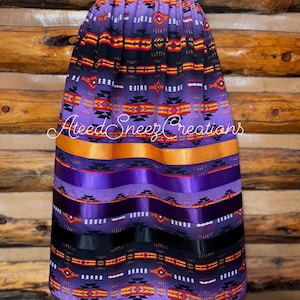 Pode incluir: Uma saia roxa com um padr&atilde;o geom&eacute;trico em preto, laranja e branco, com fitas de cetim horizontais em laranja, roxo e preto. A saia tem um c&oacute;s el&aacute;stico e apresenta o texto AteedSneezCreations no centro da imagem.
