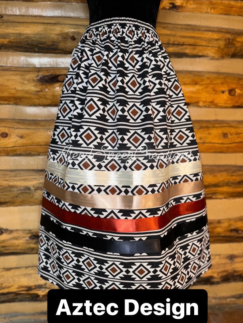Pode incluir: Uma saia at&eacute; o joelho com um padr&atilde;o geom&eacute;trico repetitivo de diamantes em preto, branco e marrom. A saia inclui detalhes de fitas de cetim horizontais em creme, bege, cobre e preto. O texto "Alesa Sheep Creations" e "Aztec Design" est&aacute; presente.
