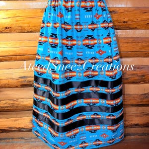 Pode incluir: Uma saia azul brilhante com um padr&atilde;o geom&eacute;trico repetitivo em preto, laranja e branco. A saia tem uma cintura el&aacute;stica e tr&ecirc;s faixas horizontais de fita preta perto da bainha. O texto AteedSneezCreations est&aacute; sobreposto na imagem.