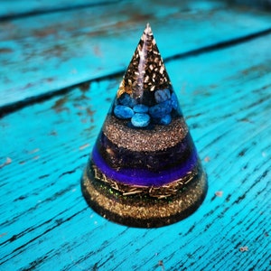 Op de afbeelding: Een gouden, blauwe en paarse kristallen piramide met een gelaagd ontwerp. De piramide is gemaakt van hars en bevat verschillende kristallen en glitter.