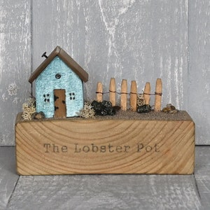 May include: A small blue wooden house with a fence and a sign that reads "The Lobster Pot" on a wooden base.