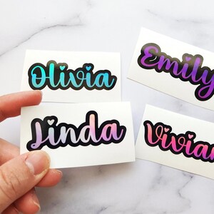 May include: Four iridescent holographic name stickers with a heart design. The names are Olivia, Emily, Linda, and Vivian.