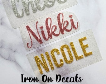 May include: Three iron-on decals with names written in glitter. The names are Chloe in silver glitter, Nikkki in rose gold glitter, and NICOLE in gold glitter.