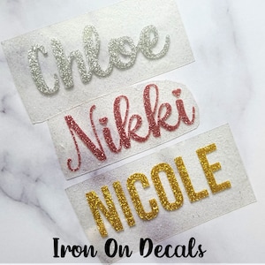 May include: Three iron-on decals with names written in glitter. The names are Chloe in silver glitter, Nikkki in rose gold glitter, and NICOLE in gold glitter.