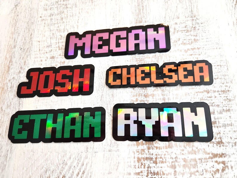 May include: Five pixelated name stickers: "Megan" in pink, "Josh" in red, "Chelsea" in orange, "Ethan" in green, and "Ryan" in silver. Each name is outlined in black and has a holographic effect.