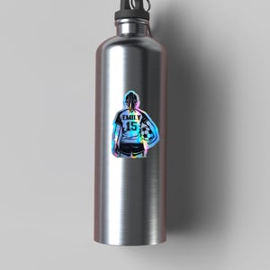May include: A stainless steel water bottle with a holographic sticker of a soccer player. The sticker shows a soccer player with the name "EMILY" and the number "15" on the back of the jersey, holding a soccer ball.