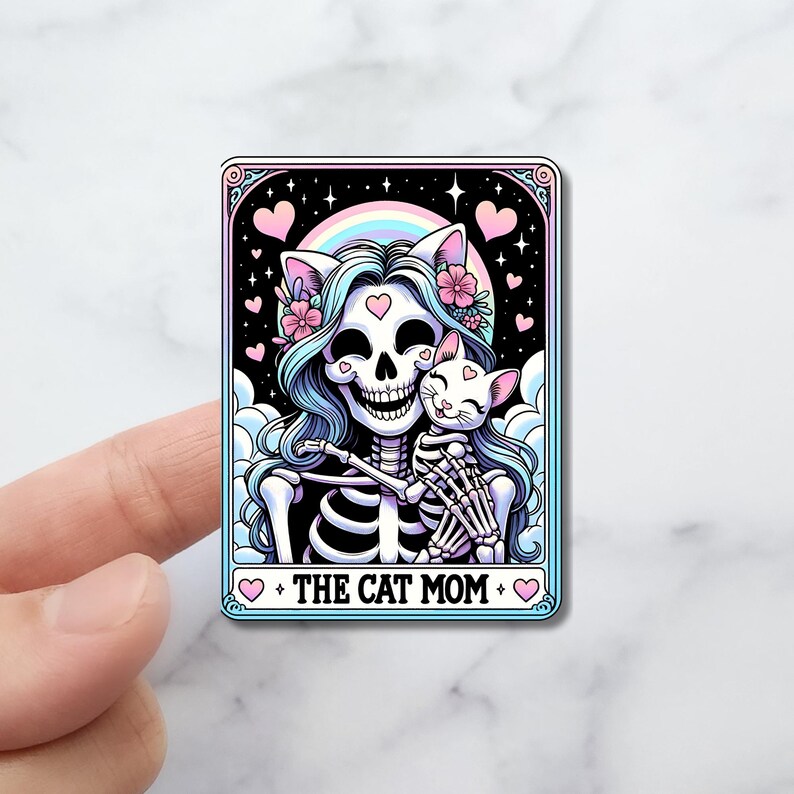 May include: A rectangular sticker featuring a skeleton with cat ears and a cat, set against a night sky with a rainbow and hearts. The text "THE CAT MOM" is at the bottom, framed by hearts.