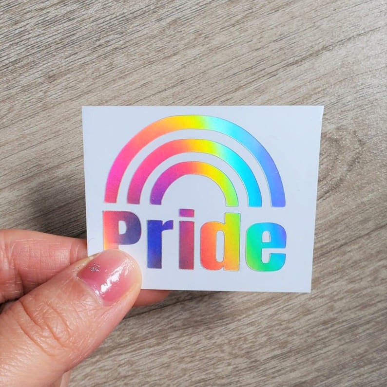 May include: A rainbow-colored vinyl sticker with the word "pride" in white letters. The sticker is on a white background.