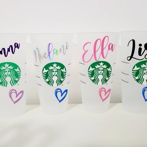 K&ouml;nnte beinhalten: Vier wei&szlig;e wiederverwendbare Becher mit schwarzem, lila, rosa und gr&uuml;nem Text. Die Becher haben ein gr&uuml;nes Starbucks-Logo mit dem Gesicht einer Frau und einem Herz in einer anderen Farbe auf jedem Becher. Die Namen Brianna, Melani, Ella und Lisa sind auf den Bechern geschrieben.