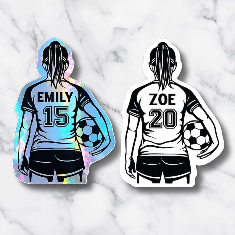 May include: Two stickers featuring a soccer player from the back, holding a soccer ball. One sticker has the name "EMILY" and the number "15" on the jersey. The other sticker has the name "ZOE" and the number "20".