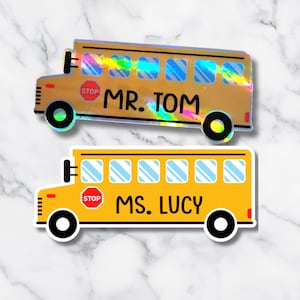 May include: Two school bus stickers. One is gold with the text "MR. TOM" and the other is yellow with the text "MS. LUCY". Both have a stop sign and black wheels.