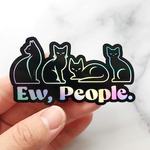 May include: A holographic sticker featuring four black cat silhouettes with a rainbow outline. The sticker has the text "Ew, People." in a gradient font, expressing a humorous sentiment about social interaction.