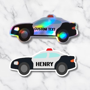 May include: Two police car stickers. One is holographic with the text "CUSTOM TEXT". The other is black and white with the name "HENRY". Both have red lights on top and are on a white background.