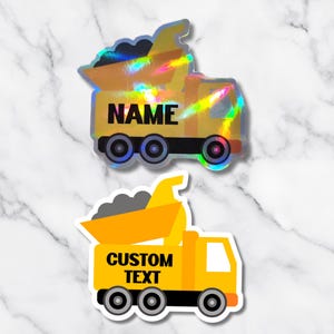 May include: Two construction truck stickers. One is holographic with the word "NAME" in black. The other is yellow with the words "CUSTOM TEXT" in black. Both have black wheels and a white border.