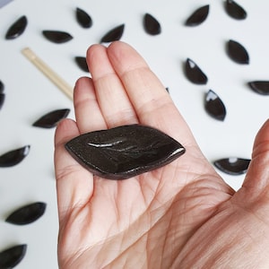 Può includere: Un piatto in ceramica nero a forma di foglia, perfetto per servire piccoli spuntini o condimenti. Il piatto è liscio e lucido, con un leggero bagliore.
