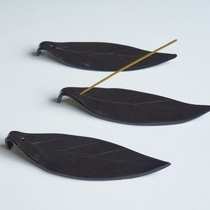 Könnte beinhalten: Drei schwarze, blattförmige Räucherstäbchenhalter aus Keramik. Die Halter sind für Räucherstäbchen konzipiert.