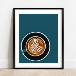 May include: A framed art print featuring a top-down view of a latte with intricate foam art. The coffee is in a teal mug on a black saucer, set against a teal background. The print is in a black frame.