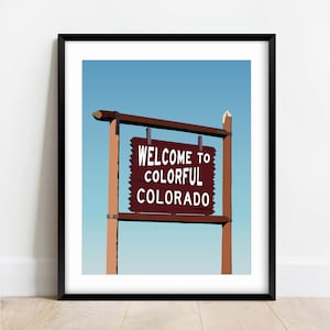 May include: A framed illustration of a wooden sign with the text "Welcome to Colorful Colorado" against a blue sky background.