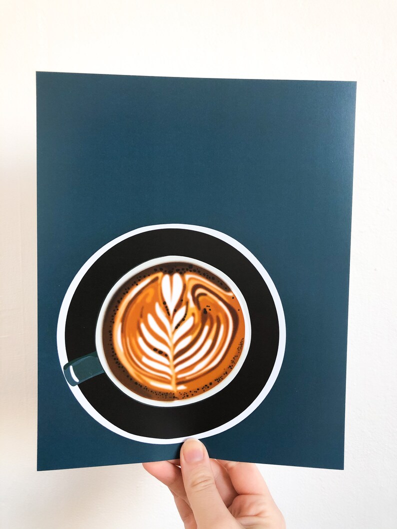 May include: A print featuring a latte art design in a black coffee cup with a teal handle, set against a dark teal background. The coffee art is a detailed leaf pattern in shades of brown and cream. The cup sits on a white circle.