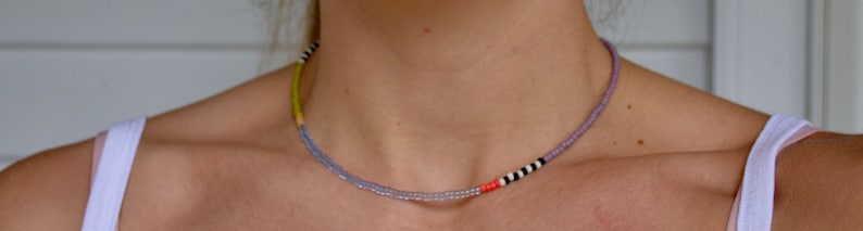 May include: A multi-colored beaded necklace with a mix of light purple, yellow, white, and black beads.