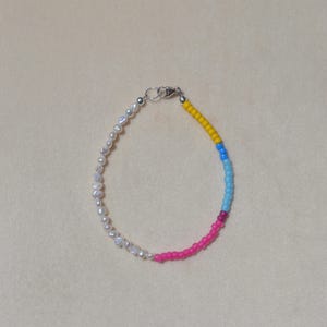 May include: A delicate bracelet featuring a combination of white pearls and colorful beads. The bracelet has a silver clasp and transitions from pearls to yellow, blue, light blue, and pink beads. A stylish accessory.