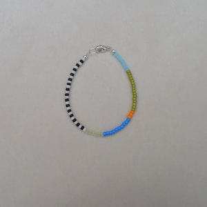 May include: A colourful beaded bracelet with black and white stripes, light green, blue, orange, and green beads.