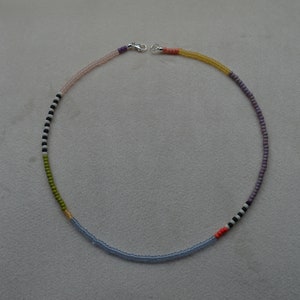 May include: A multi-colored beaded necklace with a silver clasp. The necklace is made of small beads in shades of pink, purple, green, blue, black, and white.