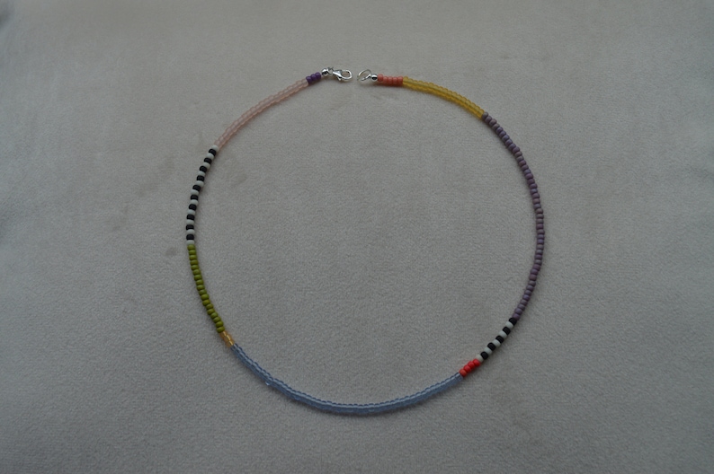 May include: A multi-colored beaded necklace with a silver clasp. The necklace is made of small beads in shades of pink, purple, green, blue, black, and white.