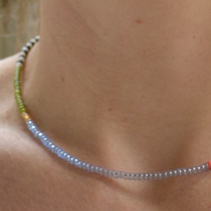 May include: A delicate choker necklace made with small, colorful beads. The necklace is a mix of light blue, white, black, and orange beads.
