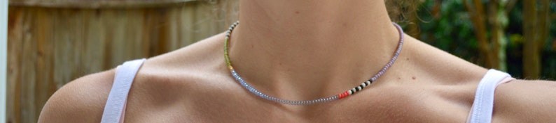 May include: A delicate choker necklace made with small, colorful beads. The necklace is a mix of light blue, white, black, and orange beads.