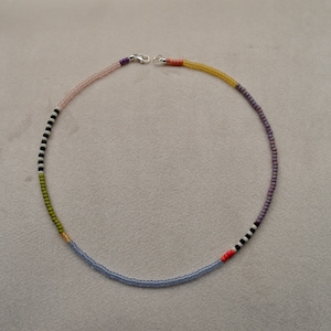 May include: A multi-colored beaded necklace with a silver clasp. The necklace features alternating colors of light pink, light blue, green, black, white, and orange.