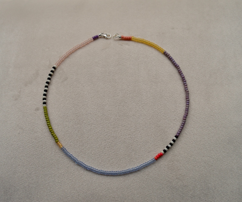 May include: A multi-colored beaded necklace with a silver clasp. The necklace features alternating colors of light pink, light blue, green, black, white, and orange.