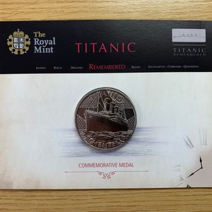 Medalha comemorativa do Titanic Remembered da Royal Mint em um cartão de exibição e uma nota de novidade do Titanic