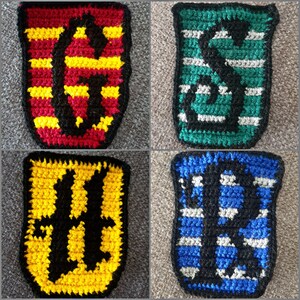 May include: Four crocheted house crests from the Harry Potter series. The crests are Gryffindor (red and gold), Slytherin (green and silver), Hufflepuff (yellow and black), and Ravenclaw (blue and bronze).