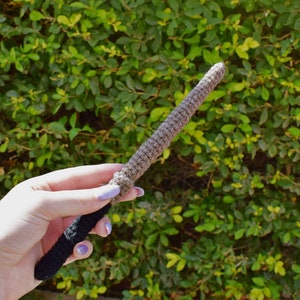 Puede incluir: Una varita de crochet de color marrón y negro. La varita se sostiene en una mano.