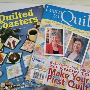 May include: Two quilting magazines are shown. One is titled "Quilted Coasters" with images of quilted coasters and coffee cups. The other is "Learn to Quilt" with photos of two women and the text "Everything You Need to Know to Make Your First Quilt."