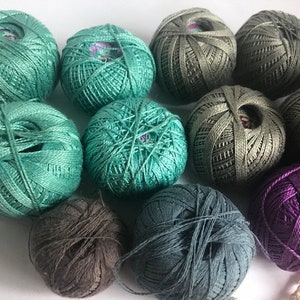 May include: A collection of yarn balls in various colors, including teal, olive green, gray, and purple. The yarn is tightly wound, and the balls are arranged closely together. The image showcases a variety of colors and textures, perfect for crafting projects.