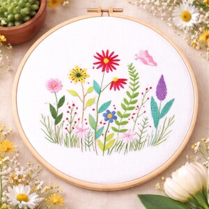 Può includere: Un telaio da ricamo circolare in legno contenente un tessuto bianco con un disegno floreale cucito a mano. Il ricamo presenta vari fiori di campo nelle tonalità del rosso, giallo, rosa, blu e viola, accompagnati da steli e foglie verdi, oltre a una piccola farfalla rosa.